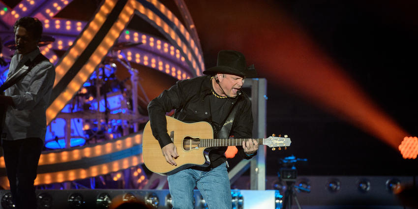 Garth Brooks plays guitar and sings to the crowd dressed in a black cowboy hat & cowboy boots in 2015.