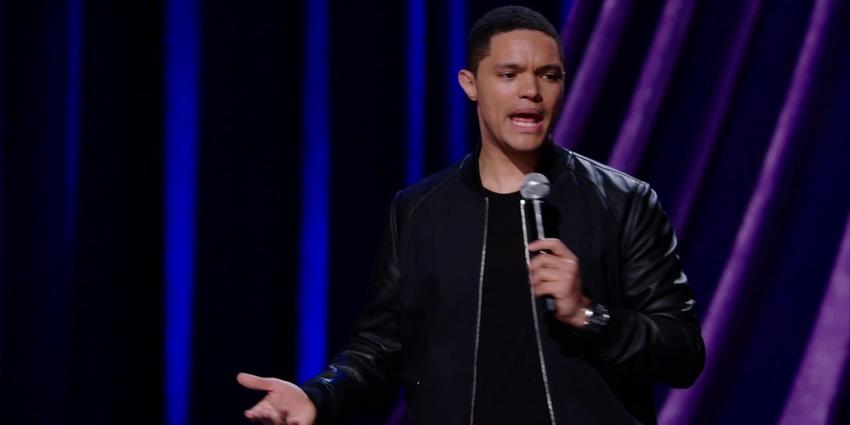 The Daily Show host, Trevor Noah, speaks into handheld microphone on stage