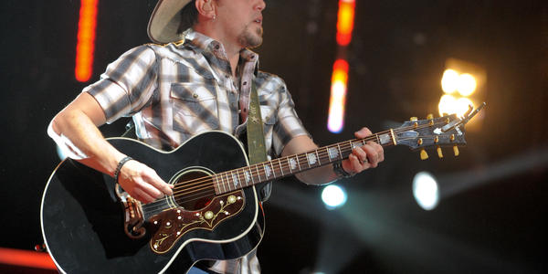 Jason Aldean performs on stage at BJC wearing his signature short sleeve plaid fitted shirt, jeans, boots & cowboy hat.