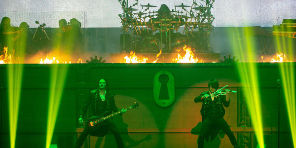 Electric guitarist and violinist perform under green lights in front of fire display on stage at BJC in 2014. 