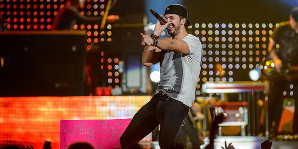 Luke Bryan, smiles and sings into handheld microphone on stage during his concert at the BJC.
