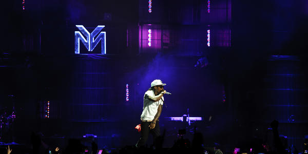 Lil' Wayne rapping into a handheld microphone on a dark stage with indigo blue stage lights shining toward the roof.