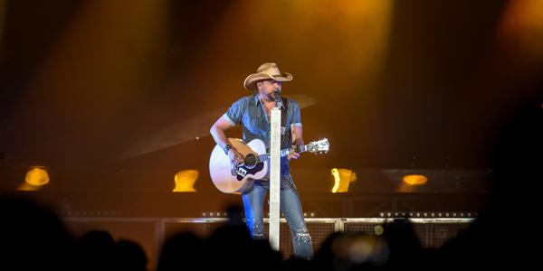 Jason Aldean, sings into standing microphone while playing guitar for the crowd at the BJC in 2014.