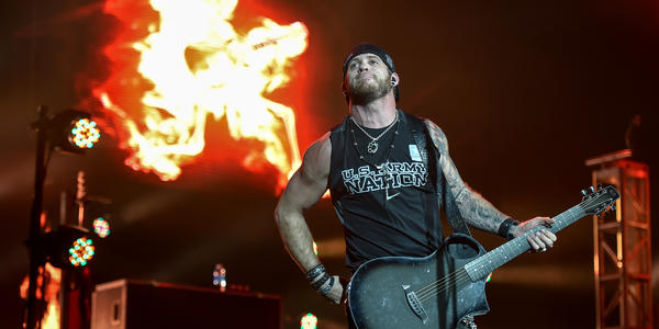 Brantley Gilbert smiles to the audience in front of staged fire in the background. 