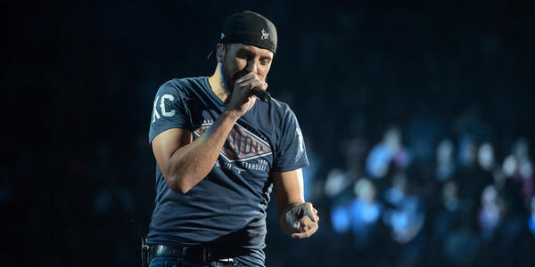 Luke Bryan, wearing a backwards baseball hat, sing into a handheld microphone to the crowd at the BJC.
