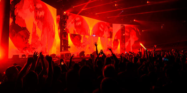 ZEDD waves to the crowd, set up in front of full stage length & height screens displaying red earths.   
