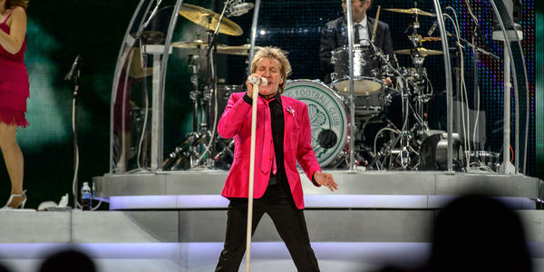 Rod Stewart, wearing a bright pink blazer & tie, sings into a white standing microphone during his concert at the BJC in 2013.
