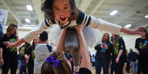 THON child, in PSU cheerleading costume, is held up in the air by a THON member.